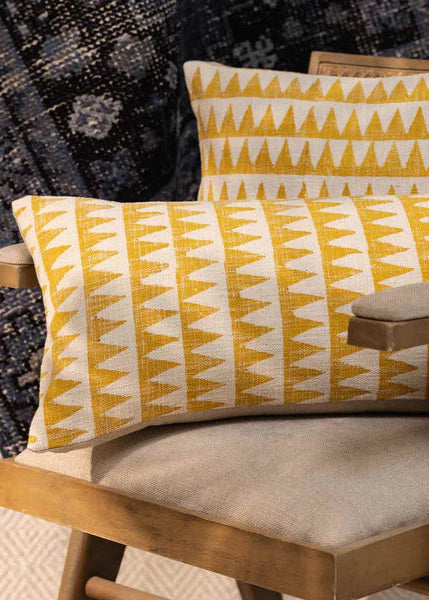 Yellow and white patterned cushions on a wooden chair with a textured wall background