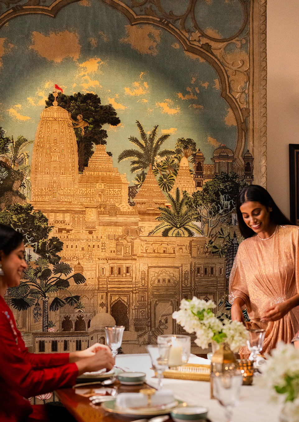 Two women sitting at a table with a decorative wall mural of a temple in the background